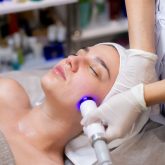 A young beautiful girl lies on the beautician's table and receives procedures with a professional apparatus for skin rejuvenation and moisturizing
